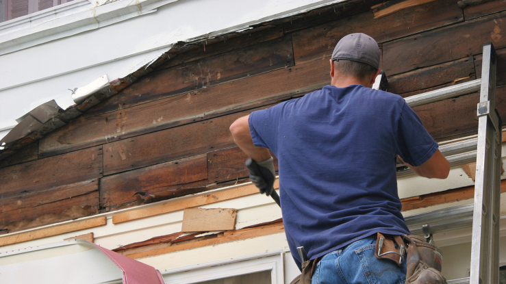 Man on a ladder removing old siding from a home.