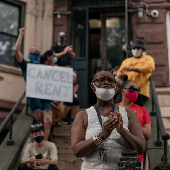People gathered on brownstone steps with "Cancel Rent" sign