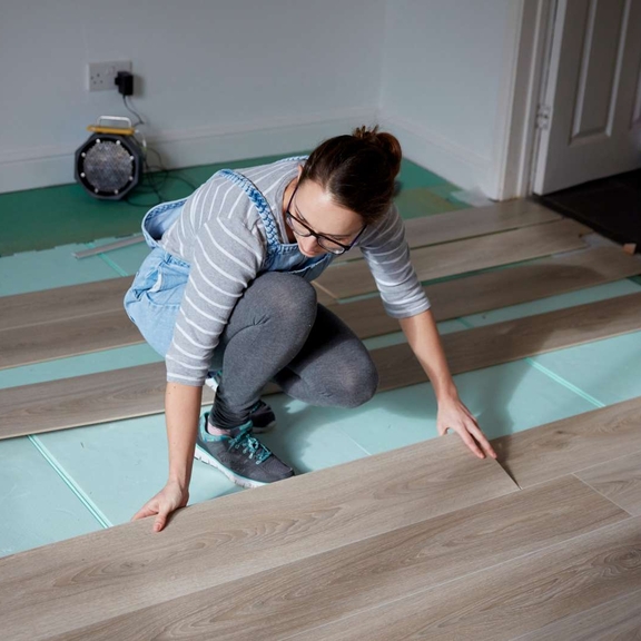 Woman laying new wood flooring.