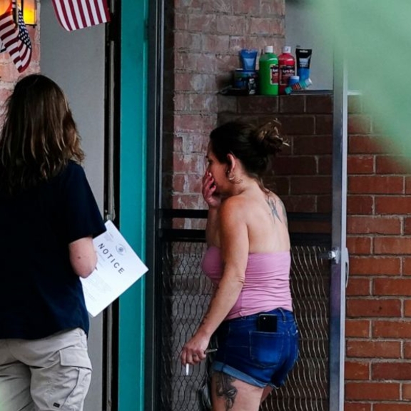Two women outside door, one holding eviction notice.