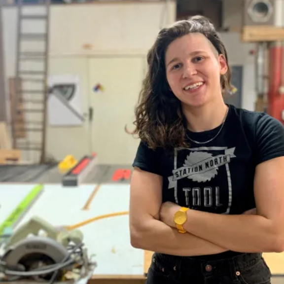 Woman with arms crossed in workshop with home improvement tools.
