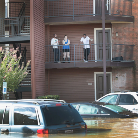 People standing on apartment building balcony above floodwaters.