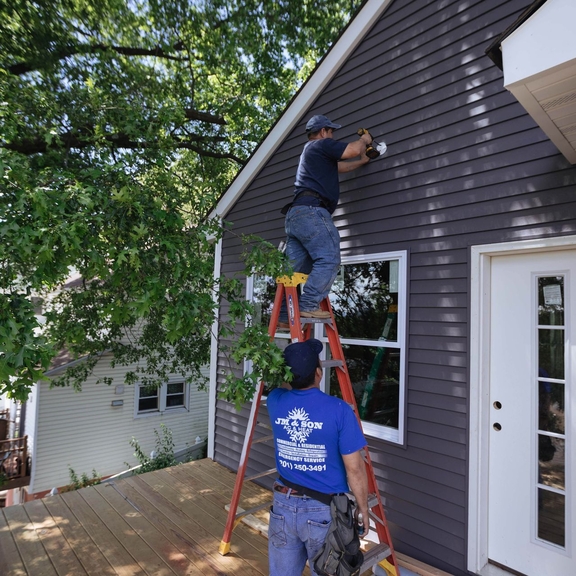 Two workers repairing the outside of a house.