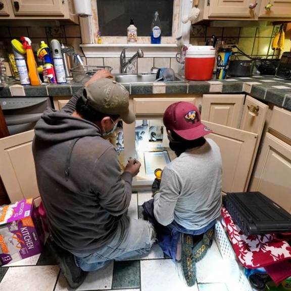 Man and boy working on pipes under sink.