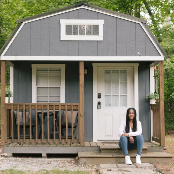 Woman sitting on front porch of tiny single-family home.