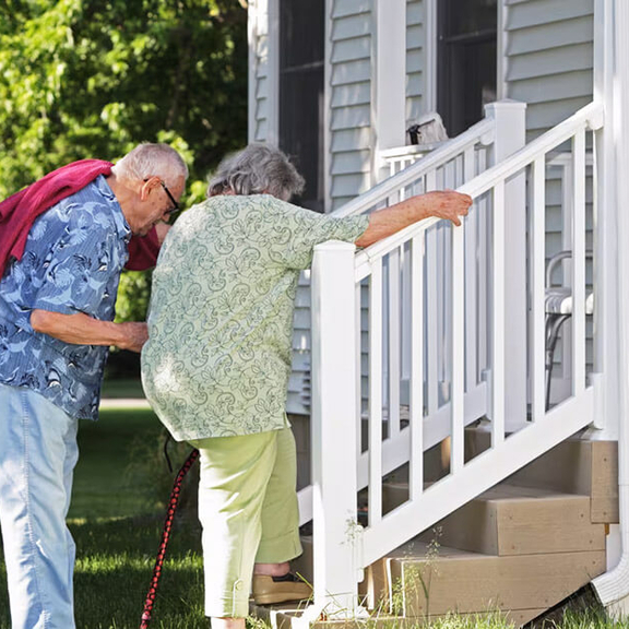 Two older adults climbing stairs to a home.