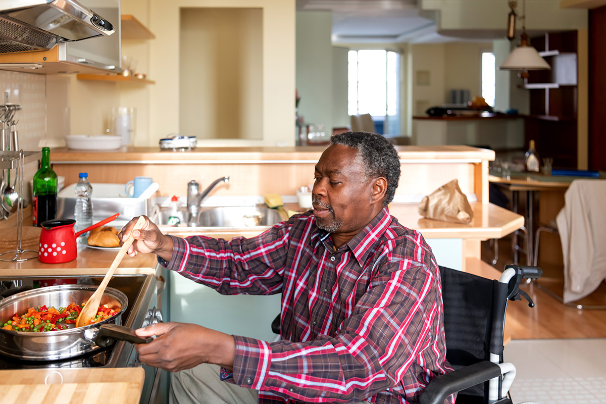 Older man in wheelchair cooking at stovetop.