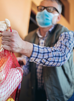 Someone handing a bag of groceries to a masked older man