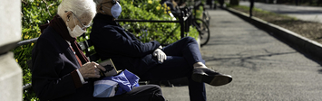 Two older adults sitting on a park bench near sidewalk.