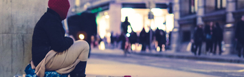 Woman experiencing homelessness sits by the sidewalk.