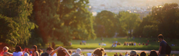 Group of young people sitting on hill overlooking city.