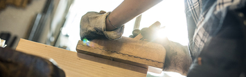 Woman shaping piece of wood in metal clamp.