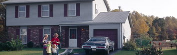 A family stands in the driveway outside their single-family house.