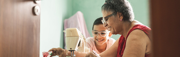 Older woman sewing at sewing machine with young boy watching.