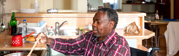 Older man in wheelchair cooking at a stovetop.