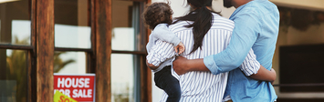 Couple with baby looking at house with "sold" sign.