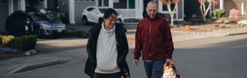 Family walking dog on suburban street.