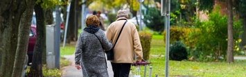 Older couple walking down sidewalk.