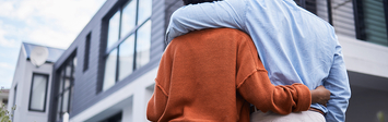 Couple standing together staring up at house.