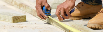 Person using measuring tape on wood beam.