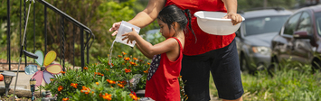 Mother and daughter watering plants in front yard.