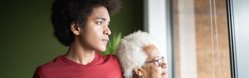 Younger man and older woman standing by window at home.