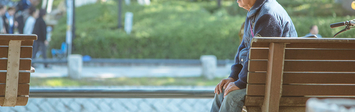 Older man sitting on bench outside.