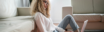 Young woman sitting on floor by couch with laptop.