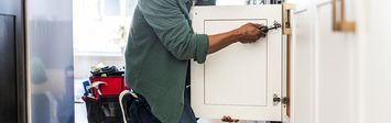 Man installing door on kitchen cabinet.