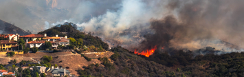Homes on a hill with wildfire in the background.