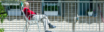 Older adult sitting on apartment balcony and looking out at neighborhood.