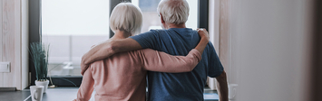 Older adult couple looking out of apartment window.